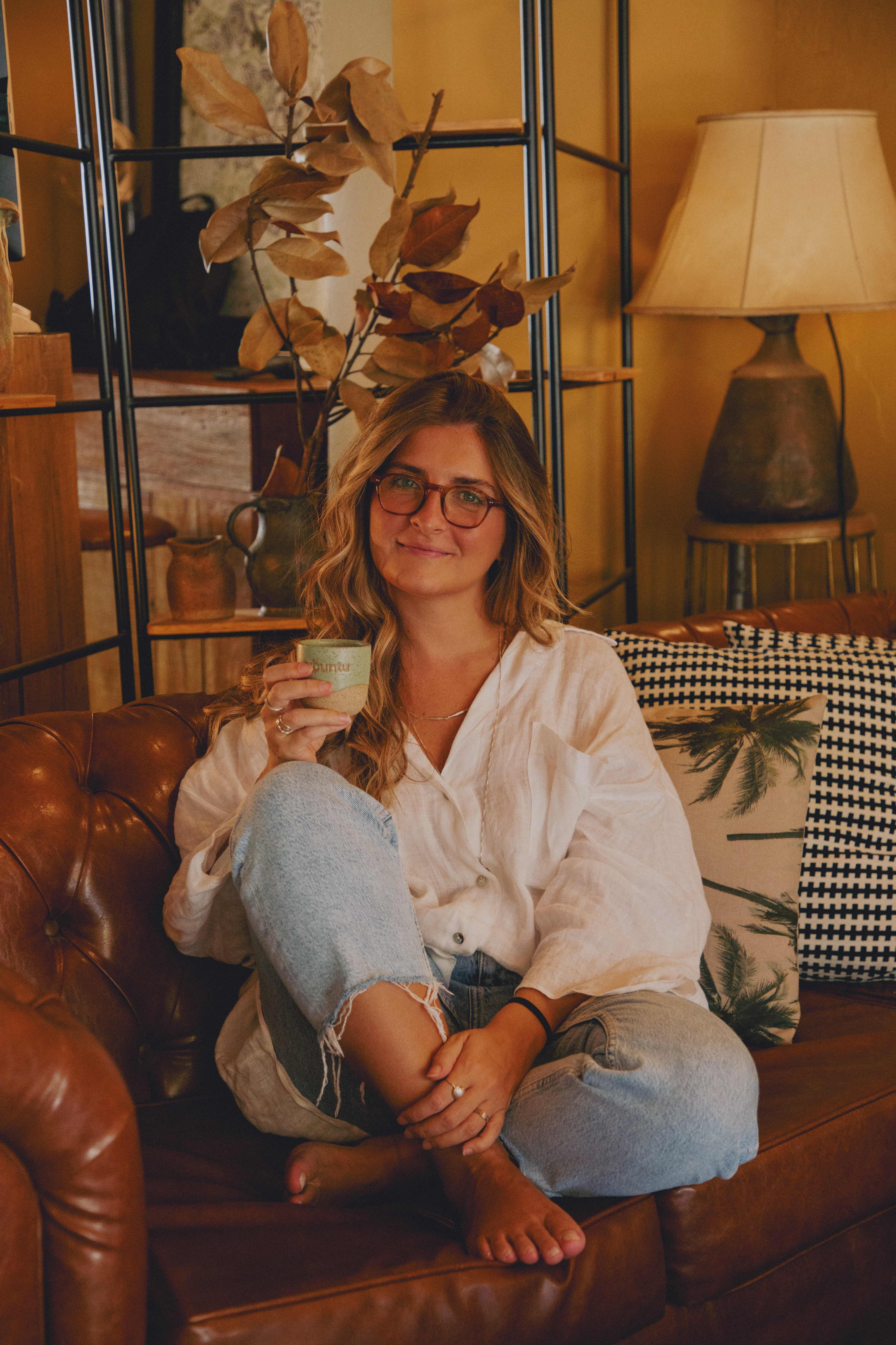 Paloma Prat, psicóloga especialista em autismo, sentada confortavelmente em um sofá de couro com uma xícara de café